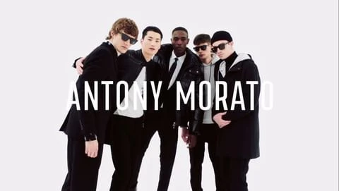 Five male models in black coats and sunglasses posing together against a plain white background with bold white text overlay.