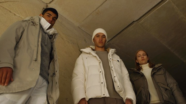 Three people pose in outerwear. Two men and one woman stand together wearing jackets and sweaters in what appears to be a tunnel or cave.