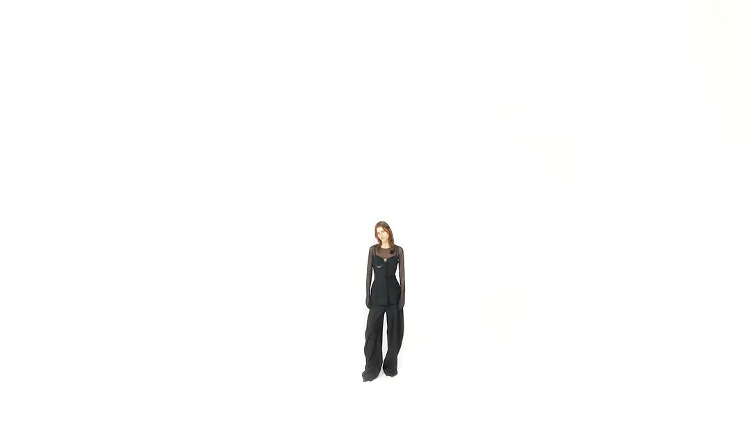 A full-length shot of an adult woman in a black outfit against a white background, showcasing contemporary fashion in a minimalist setting.