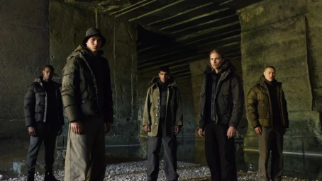 Five models in winter puffer jackets posing inside a rough stone industrial tunnel directed by Sergei Antonov