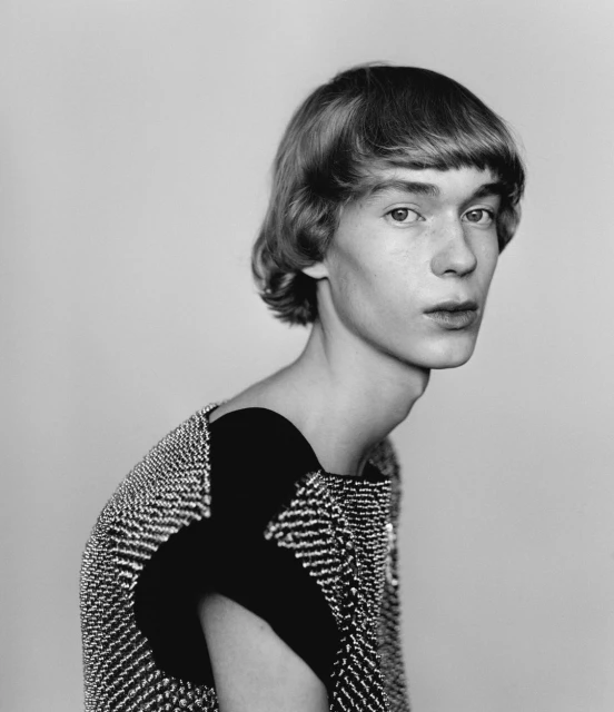 Black and white portrait of a young adult with short hair and a textured top, set against a neutral background in a studio setting.