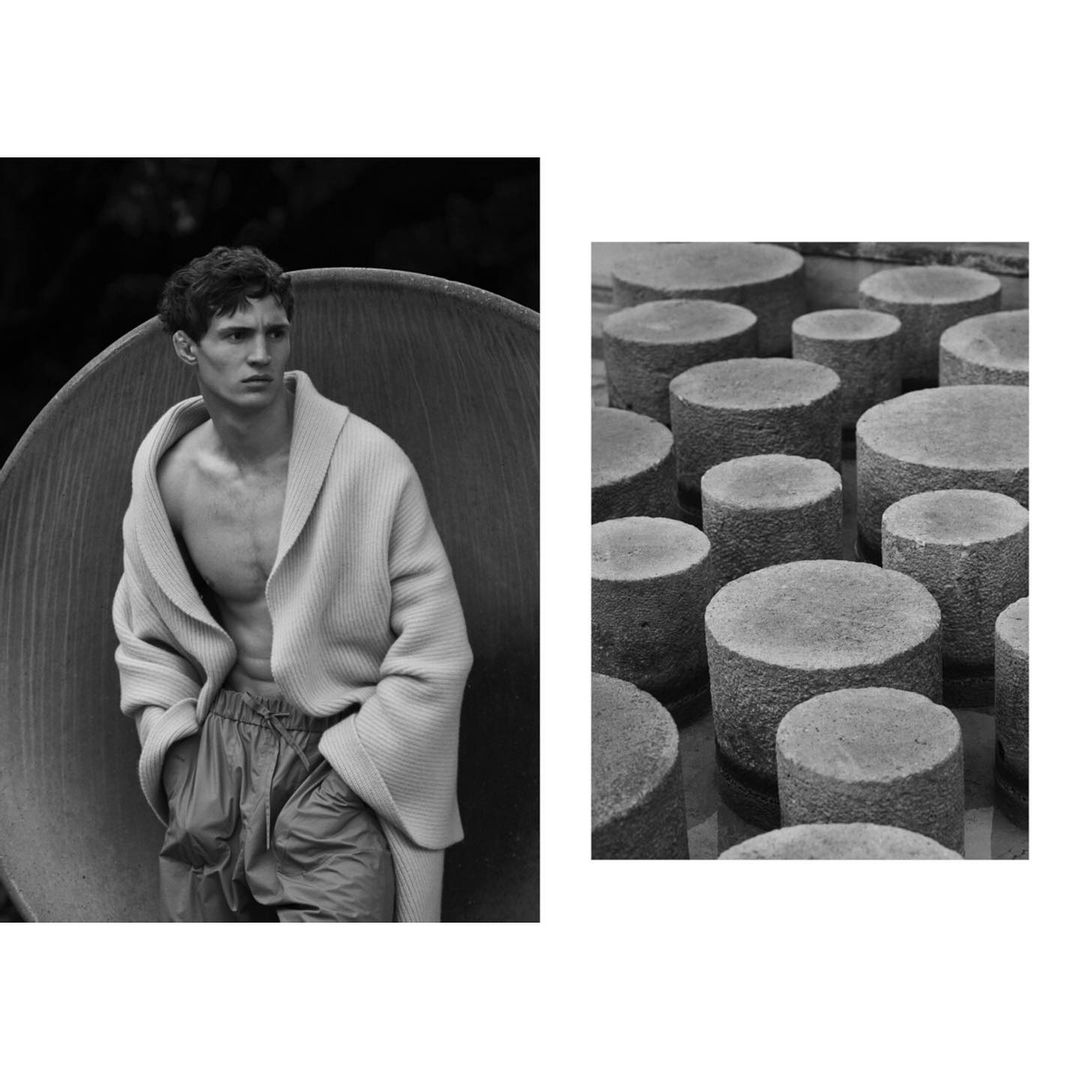 Black and white fashion shot of a male model wearing a cardigan sweater in front of a stone sculpture, paired with a concrete cylinder grid.