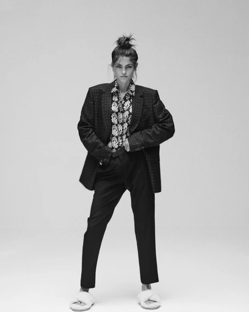 A striking black and white fashion shot of a woman in an oversized blazer, floral shirt, and fluffy slides, set against a neutral backdrop.