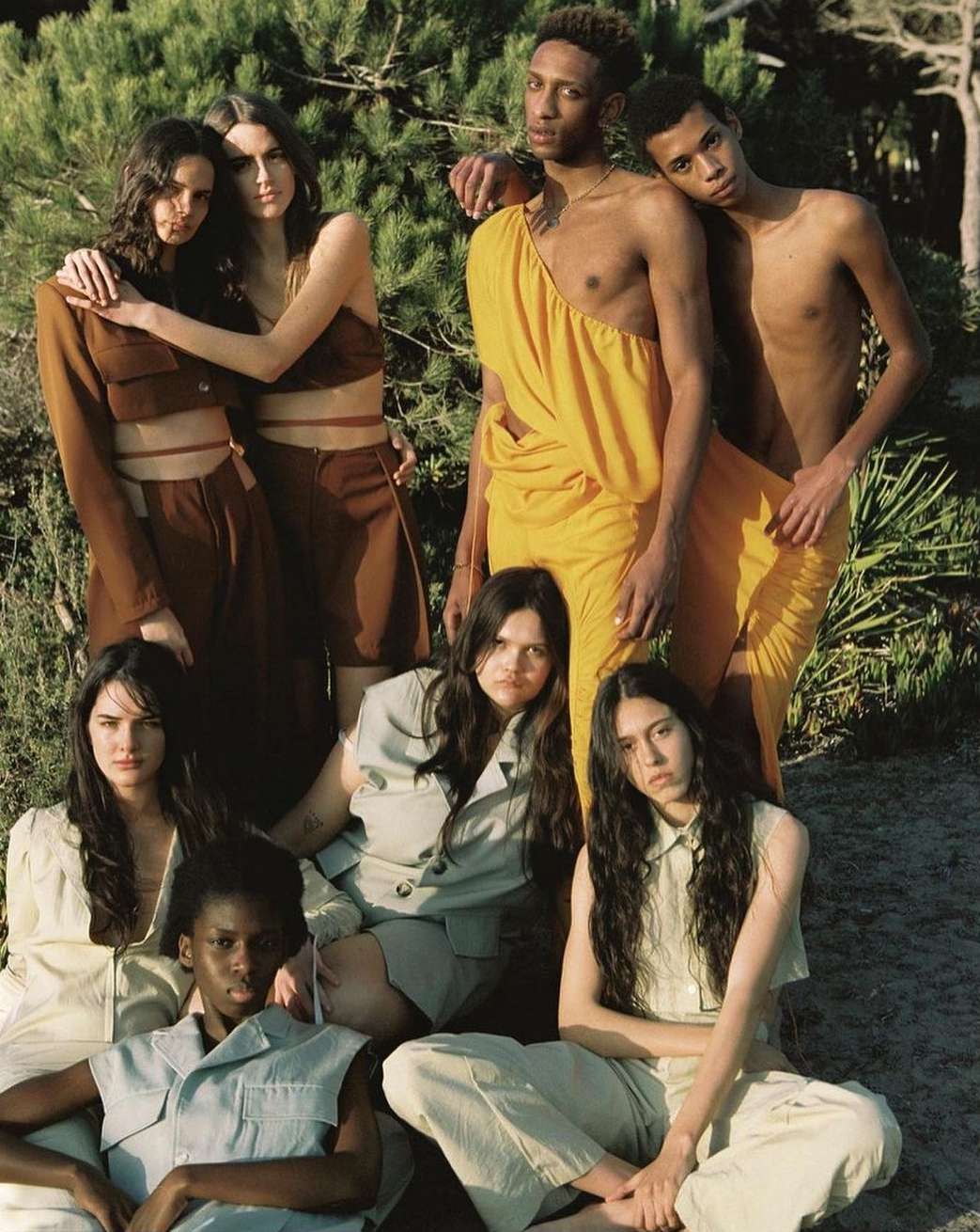 Group of seven fashion models outdoors wearing earth-tone color clothing in a casual setting with natural light.