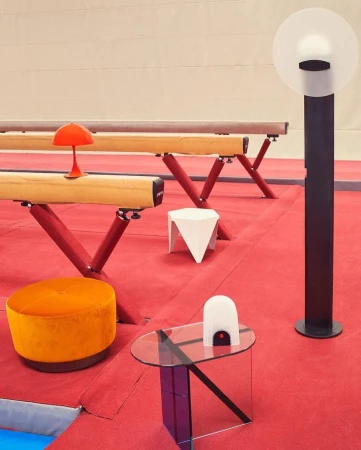 Interior design featuring a balance beam, tables, a lamp, and seating arranged on a red floor in a brightly lit indoor space.