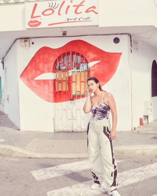Adult woman poses in front of a white building with large red lips mural and the words 'Lolita Surf Cafe' in white letters.