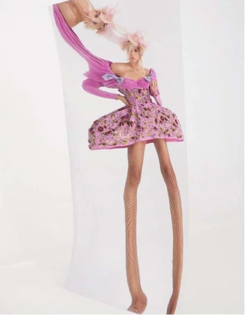 Model with exaggerated elongated legs wearing a pink patterned dress and feathered hat in a surreal vertical portrait.