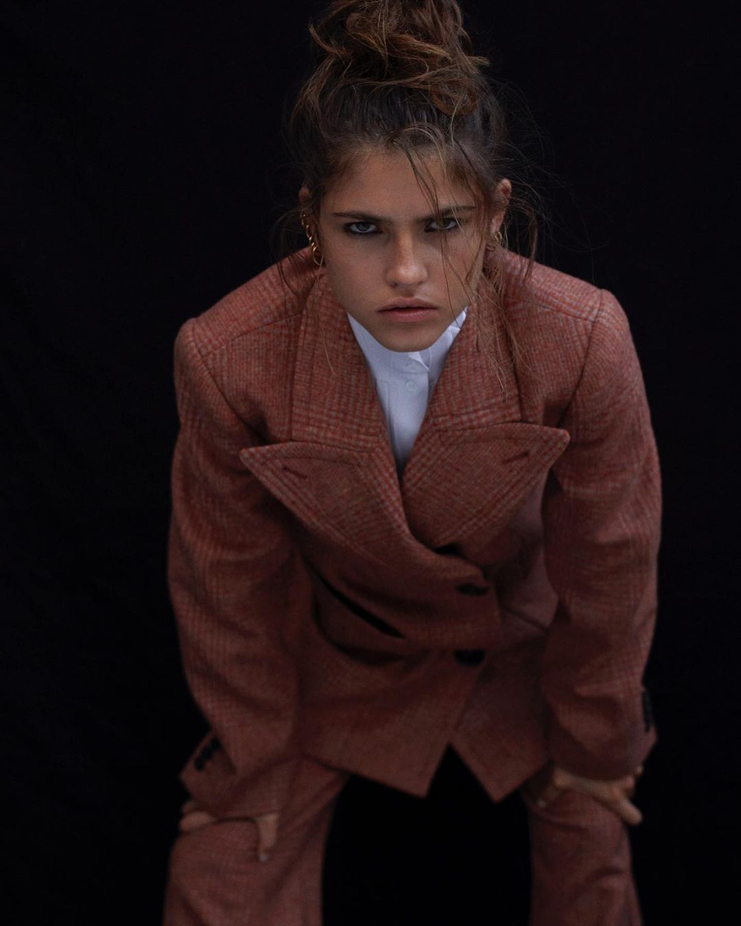 Woman in terracotta plaid blazer leaning forward against a dark background