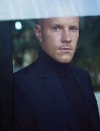 Portrait of a bald man wearing a black turtleneck and blazer, photographed by Sergi Pons.