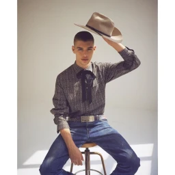 A seated male model wearing a patterned shirt, cowboy hat, and blue jeans, photographed by Sergi Pons.