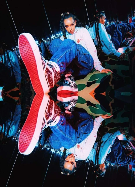 A stylish woman with braided hair sits with Vans shoes, against a reflected camouflage backdrop in cool, mirrored photo studio.