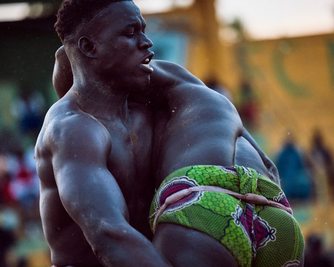 Close-up of two adult males wrestling; one is wearing a green patterned garment, showcasing a raw display of physical prowess and competition.