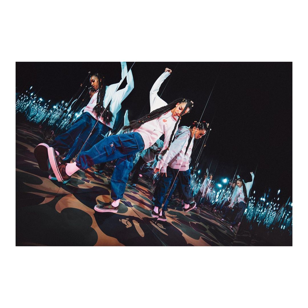 Stylish young woman in baggy jeans and sneakers strikes a pose in a modern space with reflective surfaces and blue lighting accents.