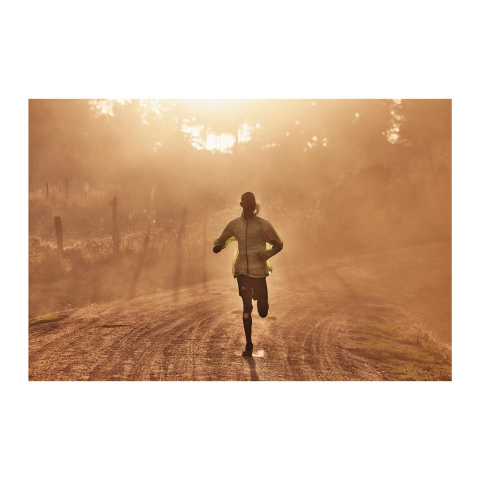 Adult male running on a dirt road in a rural environment. The scene is bathed in warm, golden light, suggesting either sunrise or sunset.