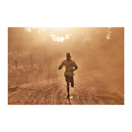 Adult male running on a dirt road in a rural environment. The scene is bathed in warm, golden light, suggesting either sunrise or sunset.