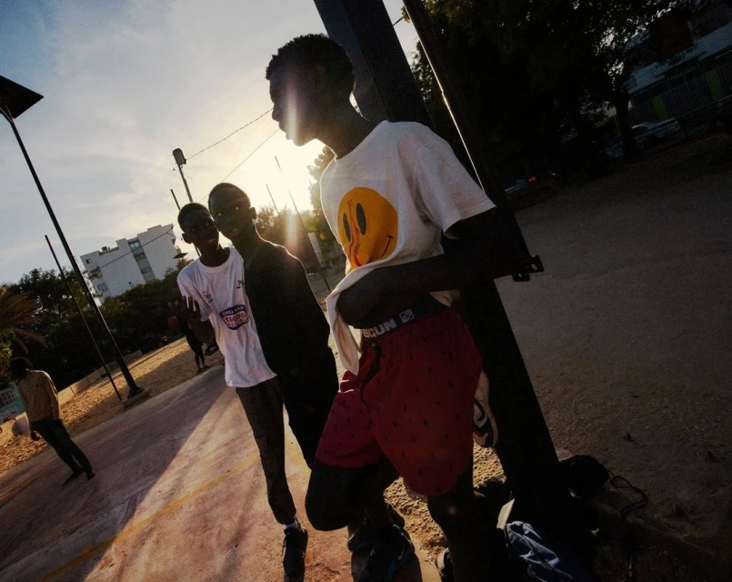Group of three young men in t-shirts and shorts in an outdoor setting, socializing and posing for the camera against the light.