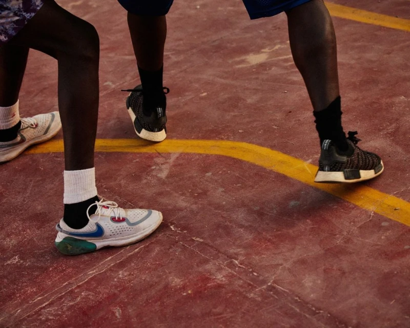 Two people in athletic footwear stand on a red and yellow outdoor court, legs visible from the knees down, showcasing sport and activity.