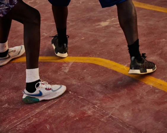 Two people in athletic footwear stand on a red and yellow outdoor court, legs visible from the knees down, showcasing sport and activity.