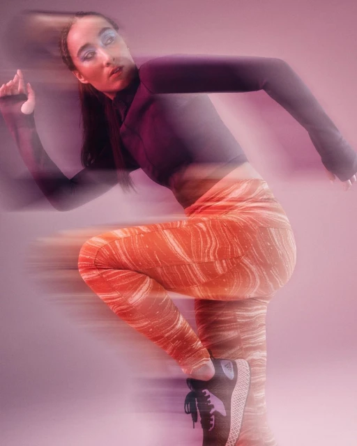 Woman in sportswear strikes a dynamic pose with motion blur against a pink background, showcasing fitness and vibrant colors.