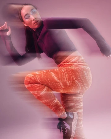 Woman in sportswear strikes a dynamic pose with motion blur against a pink background, showcasing fitness and vibrant colors.