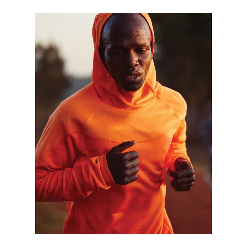 Athletic Black man running outdoors wearing an orange hooded sweatshirt. He is exercising in a natural environment in daylight.