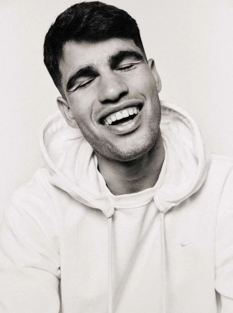 Close-up black and white portrait of a smiling adult man with closed eyes, wearing a hooded sweatshirt in an indoor setting.