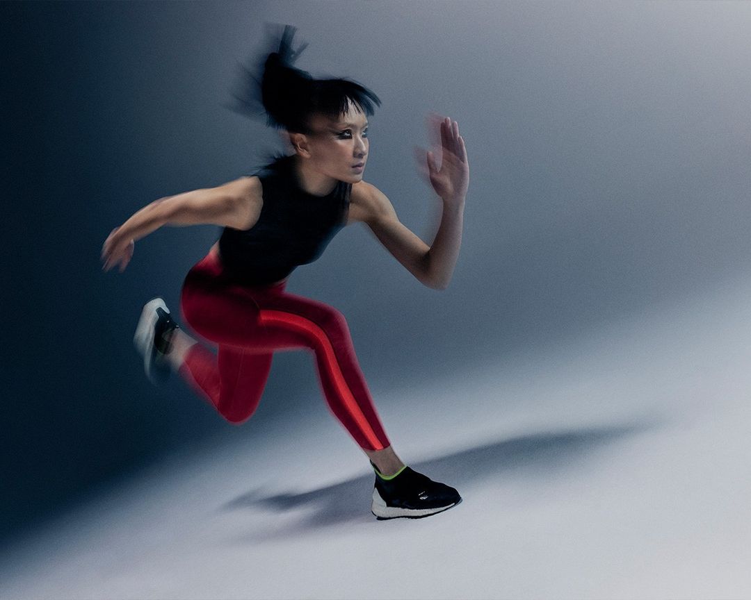 Athletic Asian woman in red leggings and black top, running in blurred motion against a blue and gray gradient background.