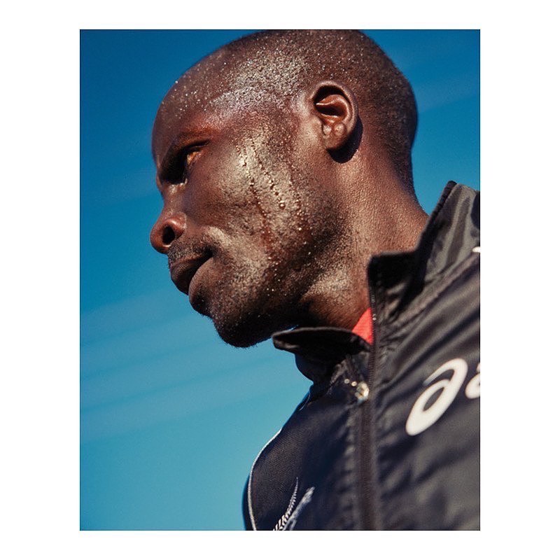 Profile of a sweaty man with dark skin wearing a jacket against a blue sky background, possibly after exercising or competing in a race.