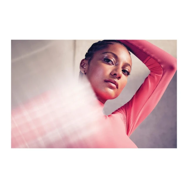 Close-up studio shot of a woman in a salmon-colored top, posing with her arm raised, soft, diffused lighting, and a modern style.