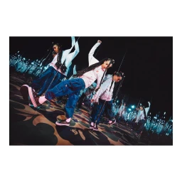 Group of dancers wearing hoodies and cargo pants performing dynamic choreography inside a dark room with illuminated walls.