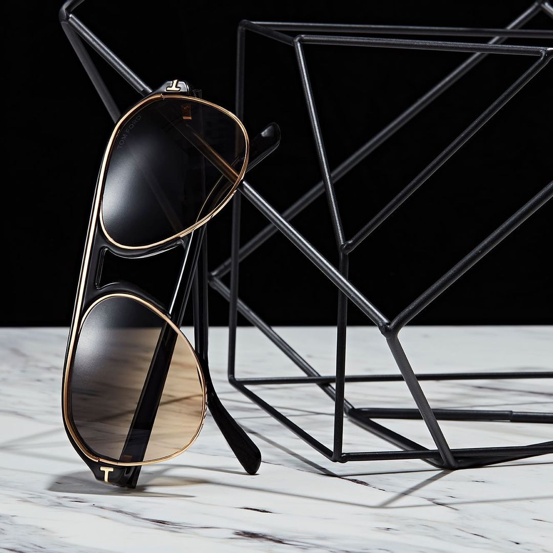 Sunglasses with gold trim leaning on a modern geometric black metal rack against a black and white marble surface.