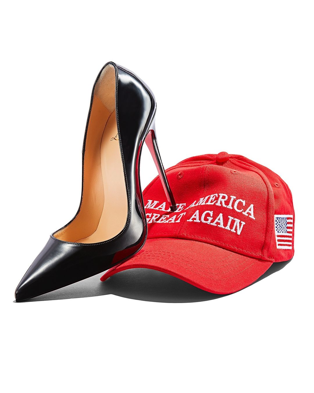 Black high heel shoe balanced on a red baseball cap with the American flag on a white background in a fashion studio shot.