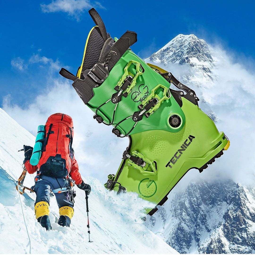 Two green and black ski boots are digitally composed over a snow-covered mountain with a climber in the lower left. 