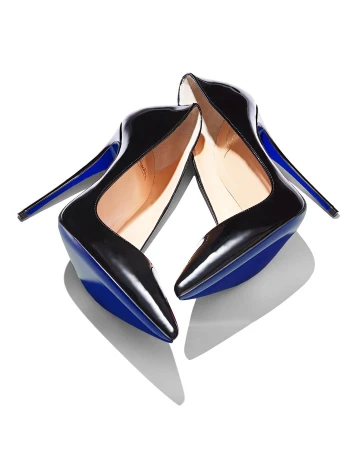 Pair of shiny black patent leather stiletto high-heeled shoes with a blue sole and stiletto heel on a white background, casting shadows.