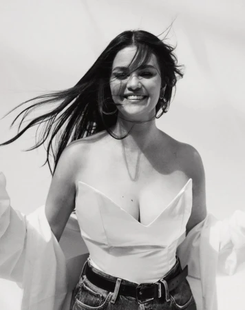 Portrait of Selena Gomez smiling with dark flowing hair in the wind wearing a white strapless top and denim jeans