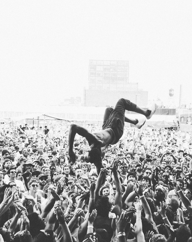Crowd surfing at a concert; a shirtless man is in mid-air, being held up by a sea of hands in a black and white photograph.