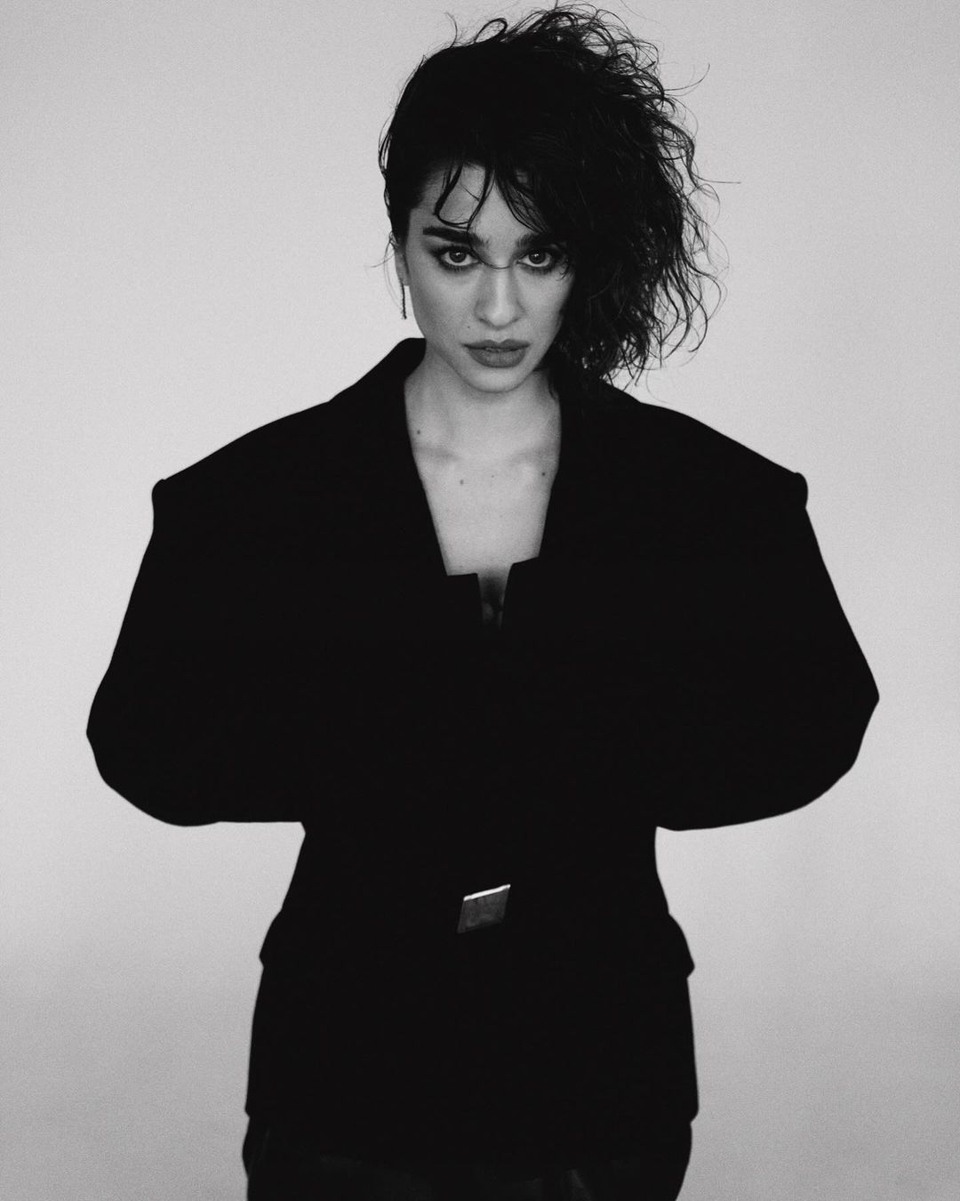 Portrait of a woman wearing an oversized black structured blazer against a plain white background by Shane Mccauley