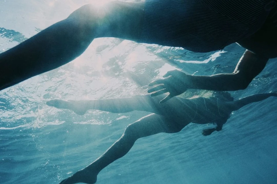 Two people swimming underwater in the ocean, sunlight filtering through the water, creating a serene and aquatic atmosphere.