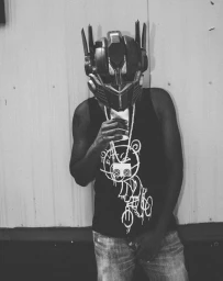 Man wearing a futuristic helmet and graphic tank top holding a cup in a black and white portrait.