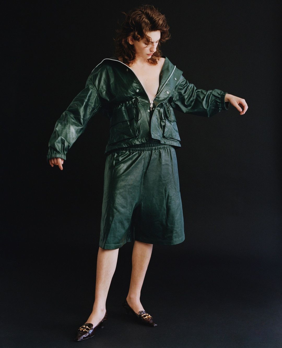 Model wearing a dark green leather jacket and matching shorts against a solid black background by Shaniqwa Jarvis.