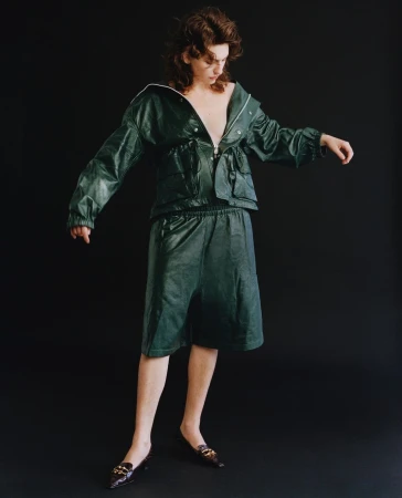 Model wearing a dark green leather jacket and matching shorts against a solid black background by Shaniqwa Jarvis.