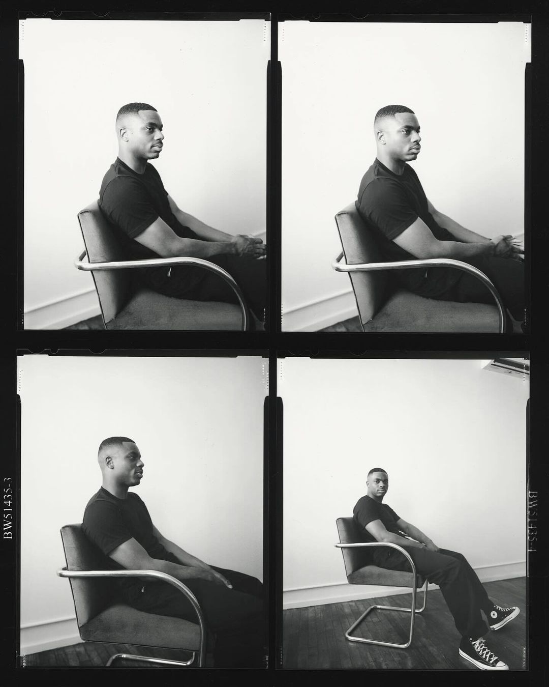 Black and white portrait of a man in a black shirt sitting in a chair with metal armrests against a bright white background.