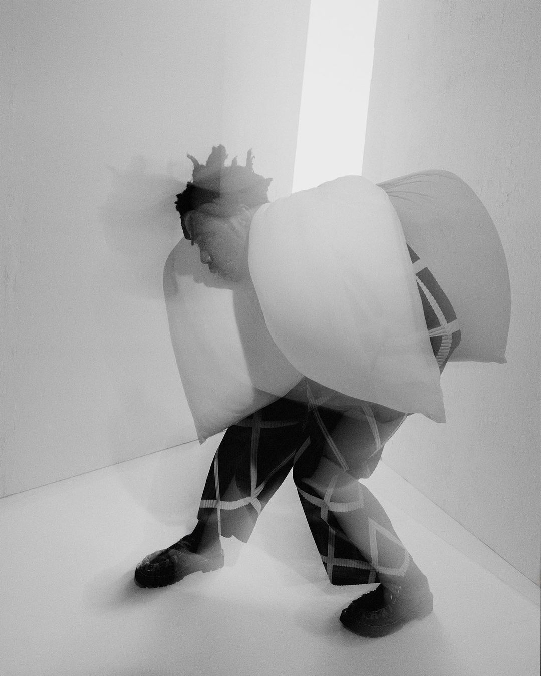 Monochrome studio shot of an adult leaning against a wall with a pillow, showcasing creative composition and minimalist background.