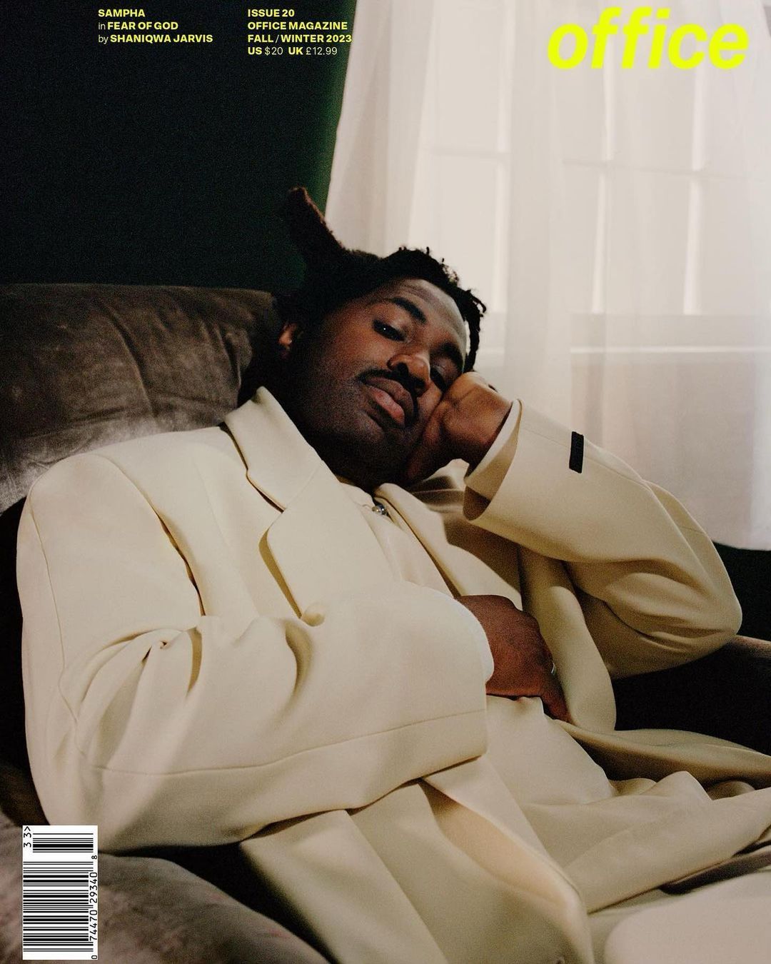 Magazine cover featuring an adult male in an off-white suit reclining on a dark green chair with the magazine's title in yellow.
