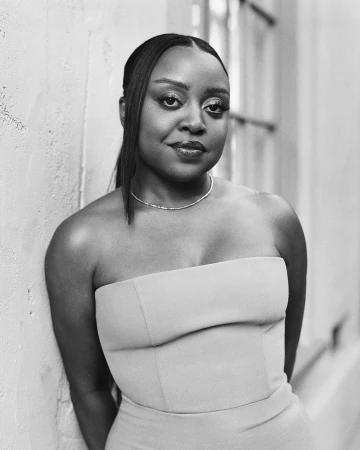 Monochrome portrait of a black woman wearing a strapless top and necklace, leaning against a textured wall.