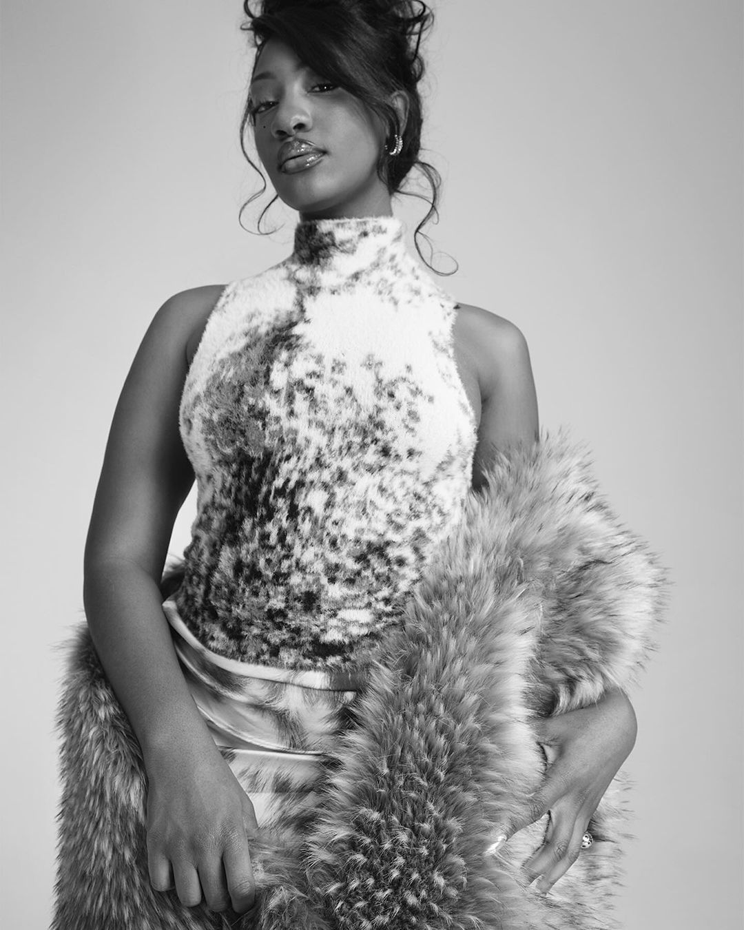 Black and white portrait of a young Black woman in a mock neck top with a fur stole, posing in front of a neutral background.