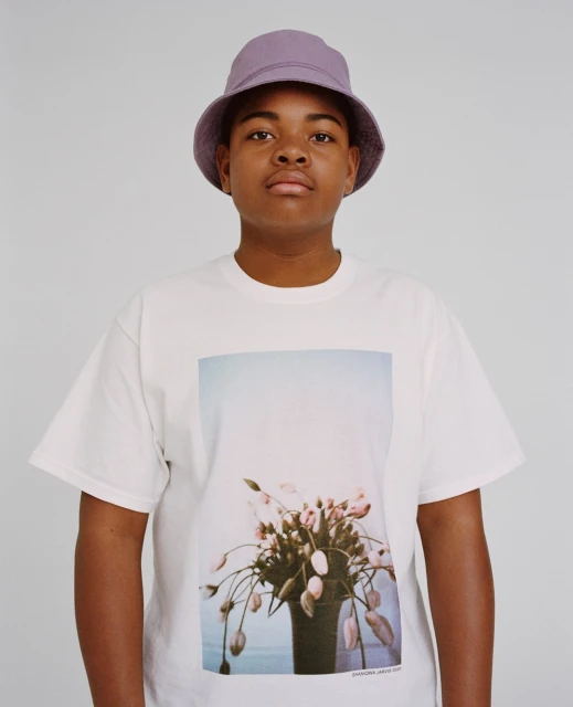 Close-up of an African-American male wearing a lavender bucket hat and a white t-shirt with a floral design posing indoors.