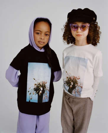 Two young girls standing side-by-side wearing graphic print t-shirts and layered clothing against a plain background