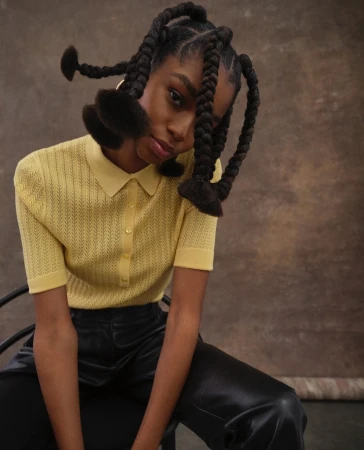 Portrait of a Black woman in a yellow polo top and black leather trousers with sculptural braided hair by Shaniqwa Jarvis.