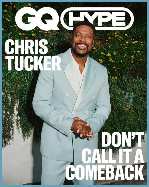 Chris Tucker in a light blue suit poses on the cover of GQ Hype magazine in front of leafy green foliage. He's smiling and looking forward.